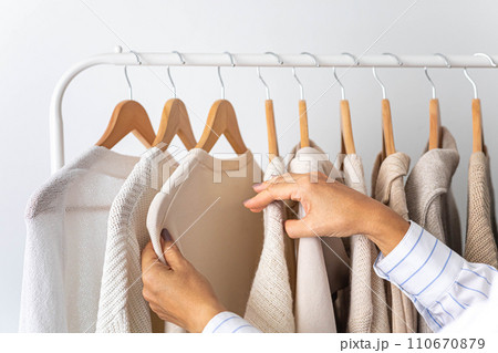 Women's hands choose neutral clothes from a hanger. White, beige and gray jersey. Women's hands choose neutral clothes from a hanger. White, beige and gray jersey. 110670879