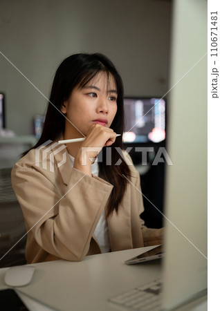 Young concentrated Asian businesswoman is working in the office, looking at her computer screen. Young concentrated Asian businesswoman is working in the office, looking at her computer screen. 110671481