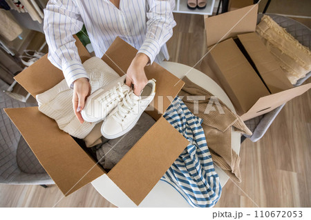 Woman packing clothes and shoes into cardboard box seasonal comfortable storage organize top view Woman packing clothes and shoes into cardboard box seasonal comfortable storage organize top view 110672053