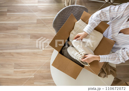 Woman packing clothes and shoes into cardboard box seasonal comfortable storage organize top view Woman packing clothes and shoes into cardboard box seasonal comfortable storage organize top view 110672072