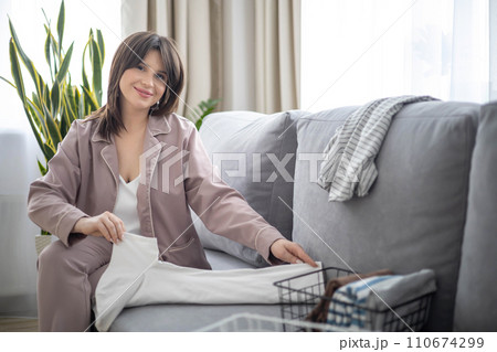 Beautiful young housewife folding linen clothes in basket comfortable storage organizing housework Beautiful young housewife folding linen clothes in basket comfortable storage organizing housework 110674299