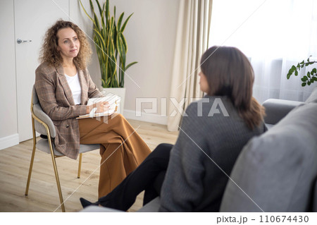 Woman psychologist talking to patient consulting at psychotherapy session making notes at office Woman psychologist talking to patient consulting at psychotherapy session making notes at office 110674430