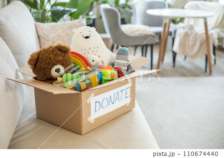 On the living room couch is a box full of toys for donation. On the living room couch is a box full of toys for donation. 110674440