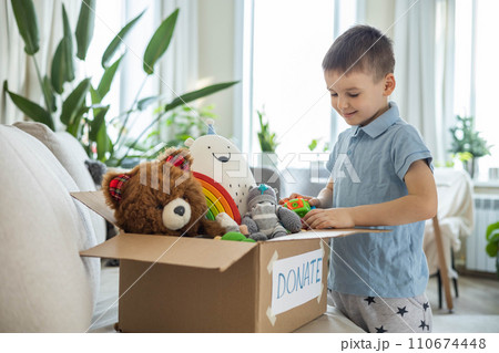 Boy child puts toys in a cardboard box for charity. Donation concept. 110674448