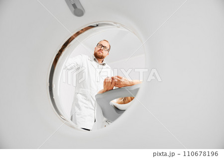 Medical computed tomography or MRI scanner. Male radiologist presses MRI button to examine female patient. Concept of healthcare and modern diagnostics. Medical computed tomography or MRI scanner. Male radiologist presses MRI button to examine female patient. Concept of healthcare and modern diagnostics. 110678196