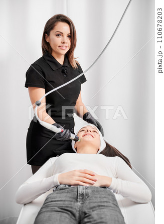 Medical esthetician cosmetologist using radiofrequency device while performing rejuvenation facial treatment in cosmetology clinic. Woman having skincare face lifting procedure in beauty salon. 110678203