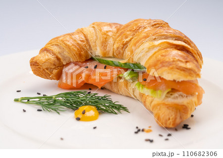 Breakfast. Croissant with salmon and vegetables on a white plate and a white background Breakfast. Croissant with salmon and vegetables on a white plate and a white background 110682306