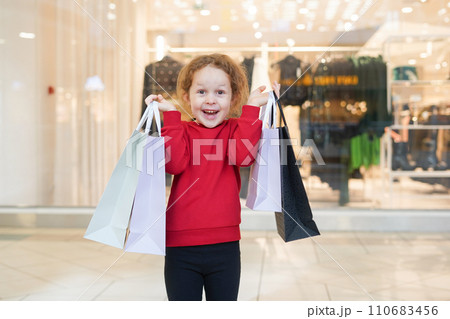 Happy child girl in red sweater with shopping bags in cloth store. Black Friday concept 110683456