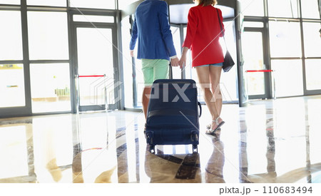 Couple dressed in luxury suits, leave hotel hall with suitcases Couple dressed in luxury suits, leave hotel hall with suitcases 110683494