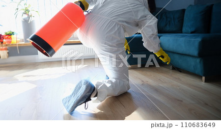Person in hazmat suit disinfects living room with spray gun 110683649
