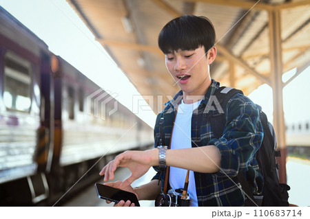 Male traveler with backpack checking time while waiting for train at platform. Male traveler with backpack checking time while waiting for train at platform. 110683714