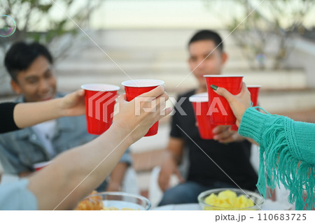 Friendship and celebration and lifestyle concept. Group of adult friends clinking plastic cups on rooftop party Friendship and celebration and lifestyle concept. Group of adult friends clinking plastic cups on rooftop party 110683725