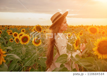 Woman in Sunflower Field: Happy girl in a straw hat posing in a vast field of sunflowers at sunset, enjoy taking picture outdoors for memories. Summer time. 110684584