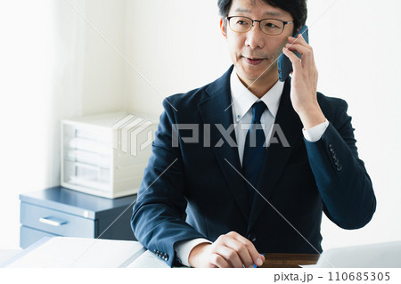 パソコンを見ながらスマホで通話するビジネスマン 110685305