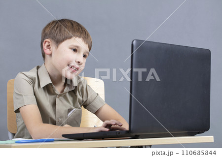 The child at the laptop. The boy looks at the monitor screen. Preschooler at the computer. Junior student at a table with a computer. The child at the laptop. The boy looks at the monitor screen. Preschooler at the computer. Junior student at a table with a computer. 110685844