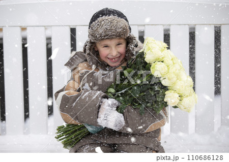 Child in the winter on the street with a bouquet of flowers. Funny boy in cold weather with an armful of roses. 110686128