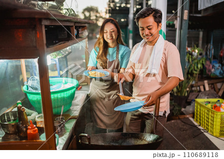 indonesian female helping male seller cooking fried rice 110689118
