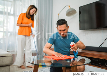 asian male spraying and wiping table while cleaning house asian male spraying and wiping table while cleaning house 110689327