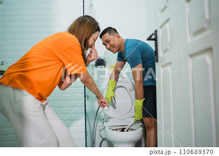 asian man wearing gloves cleaning toilet bowl 110689370