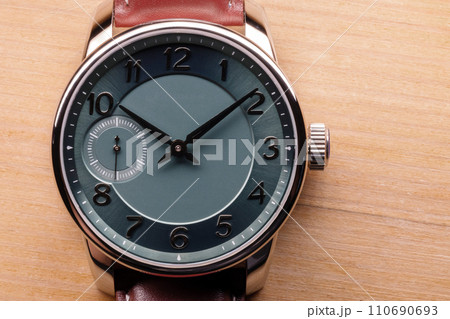 Gents wrist watch with green clock face lays on a wooden table 110690693