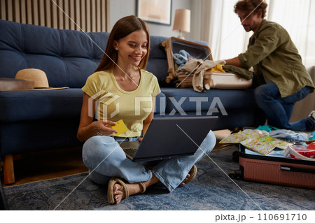 Wife booking ticket paying for hotel while husband preparing luggage for trip Wife booking ticket paying for hotel while husband preparing luggage for trip 110691710