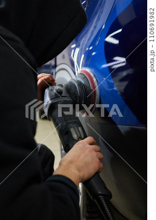 Man with an orbital polisher in car workshop polishing car closeup 110691982