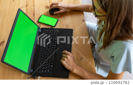 Top view young girl working or studying using her laptop and smartphone with mock up green screens. Top view young girl working or studying using her laptop and smartphone with mock up green screens. 110692762