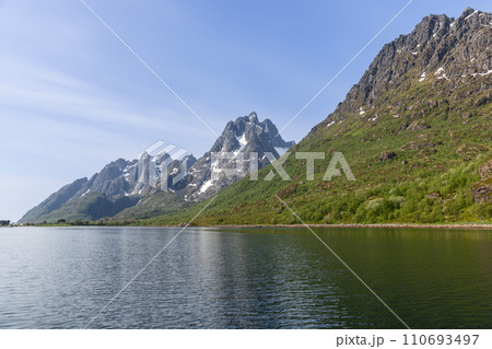 Tranquil Lofoten waters mirror towering peaks with winter remnants under Norway's sky 110693497