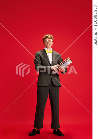 Personal assistance. Young guy, employee standing in formal wear, holding business folders against red studio background 110693537