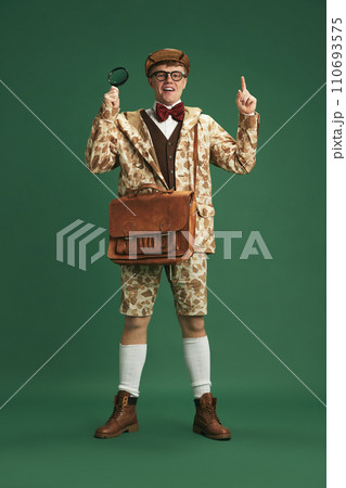 Full-length image of young guy wearing retro clothes of detective, standing against green studio background 110693575