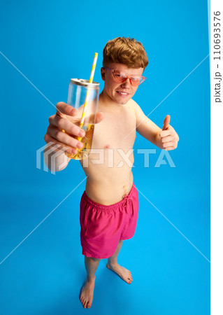 Portrait of young redhead man in stylish pink sunglasses standing with lemonade against blue studio background. Enjoyment Portrait of young redhead man in stylish pink sunglasses standing with lemonade against blue studio background. Enjoyment 110693576