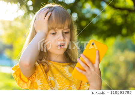 Surprised child girl play game use smartphone loses, bad news, fortune loss fail on city park street Surprised child girl play game use smartphone loses, bad news, fortune loss fail on city park street 110693799