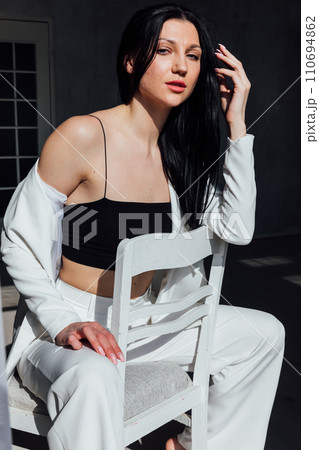 Beautiful fashionable slender brunette woman sitting on a chair Beautiful fashionable slender brunette woman sitting on a chair 110694862