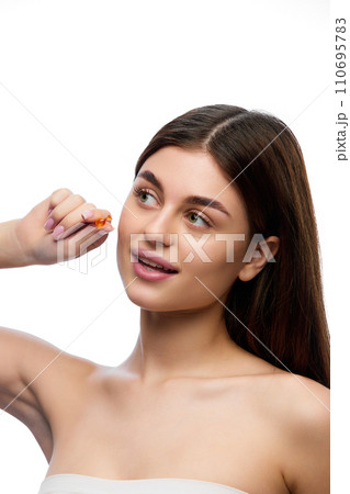 Portrait of naturally beautiful, brunette woman with perfect long, silky and healthy hair showing hair-care oil capsule and looking away. 110695783