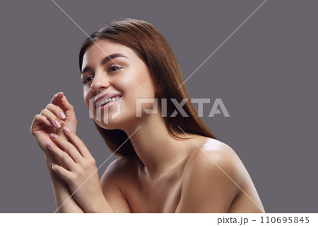 Portrait of young brunette woman with pleasant appearance posing and smiling against grey studio background. Concept of natural beauty people. Portrait of young brunette woman with pleasant appearance posing and smiling against grey studio background. Concept of natural beauty people. 110695845