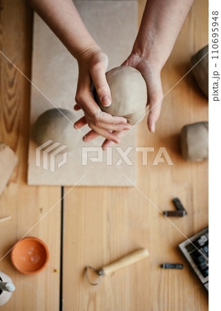 Ceramist Slapping a damp lump of clay with his hands. Round lump of raw white clay in hands Preparing for clay modeling in a workshop, top view Ceramist Slapping a damp lump of clay with his hands. Round lump of raw white clay in hands Preparing for clay modeling in a workshop, top view 110695948