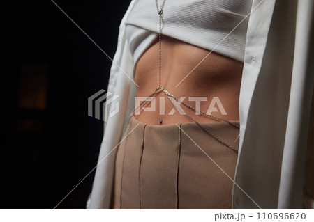 woman with a silver waist chain. A girl in a white top, a belly chain with heart details and her hand in a pocket woman with a silver waist chain. A girl in a white top, a belly chain with heart details and her hand in a pocket 110696620