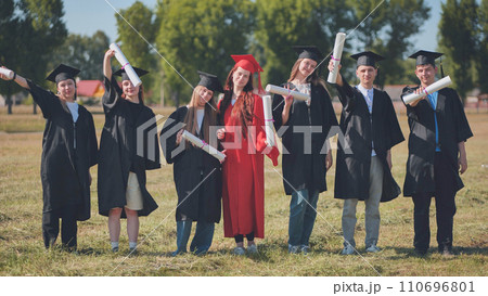 Young graduates pose with diplomas in hand on the street. 110696801