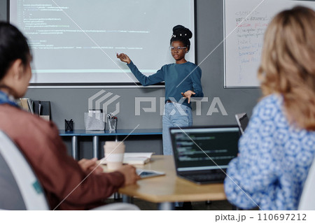 Black female office employee pointing on digital screen with codes, her female coworkers listening 110697212