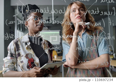 Two biracial female programmers writing code on glass board in modern IT company office Two biracial female programmers writing code on glass board in modern IT company office 110697234