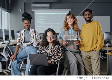 Diverse group of young programmers posing together at office holding gadgets and smiling at camera 110697238