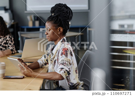 Side view shot of young black girl with dreadlocks working on tablet sitting at office desk 110697271