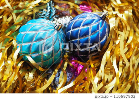Christmas balls, foil cones and decorations with gold tinsel close-up. Beautiful bright decorative balls of a modern fashionable design with intertwining stripes. New Year's and Christmas Xmas Christmas balls, foil cones and decorations with gold tinsel close-up. Beautiful bright decorative balls of a modern fashionable design with intertwining stripes. New Year's and Christmas Xmas 110697902