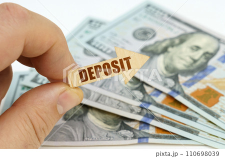 In the hands of a man is an arrow with the inscription - DEPOSIT, in the background there are dollars. In the hands of a man is an arrow with the inscription - DEPOSIT, in the background there are dollars. 110698039