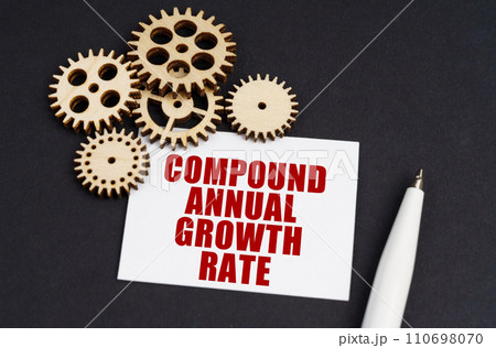 On the black surface are gears, a pen and a business card with the inscription - Compound Annual Growth Rate 110698070