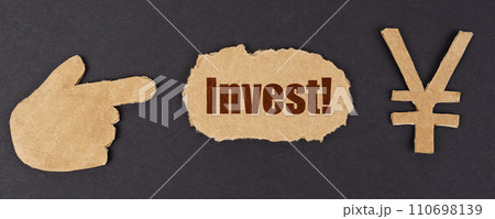 On a black surface, a figure of a hand, a yen symbol and a torn cardboard with the inscription - Invest 110698139