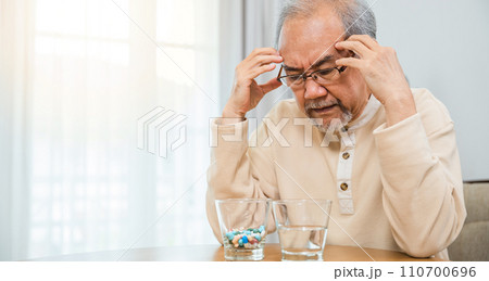Asian senior old man grey haired sad sitting in chair hand hold head with many medicines and pills for taking, elderly man sick have headache looking pill glass on at home, Elderly healthcare Asian senior old man grey haired sad sitting in chair hand hold head with many medicines and pills for taking, elderly man sick have headache looking pill glass on at home, Elderly healthcare 110700696