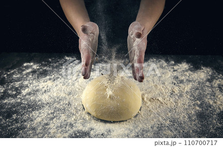 Chef sprinkles white wheat flour on fresh dough on a dark background. Food concept. Chef sprinkles white wheat flour on fresh dough on a dark background. Food concept. 110700717
