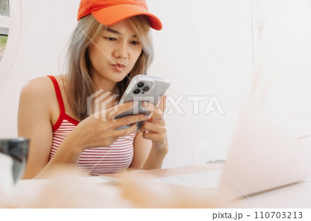 Cute freelance girl is using smartphone while working on laptop. 110703213