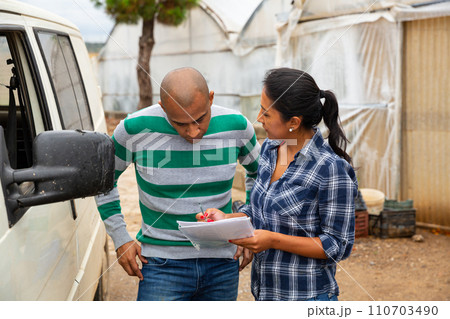 Woman and man discussing documents on farm near car 110703490